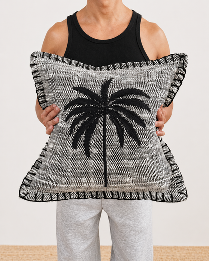 Person holding a decorative pillow with a palm tree design on a plain background