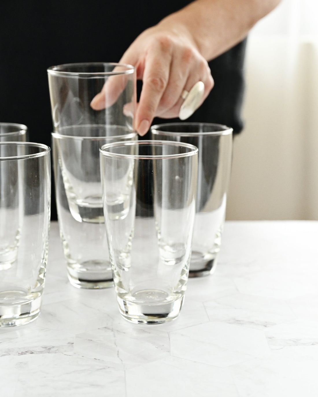 Clear glasses on a marble surface with a hand reaching in.