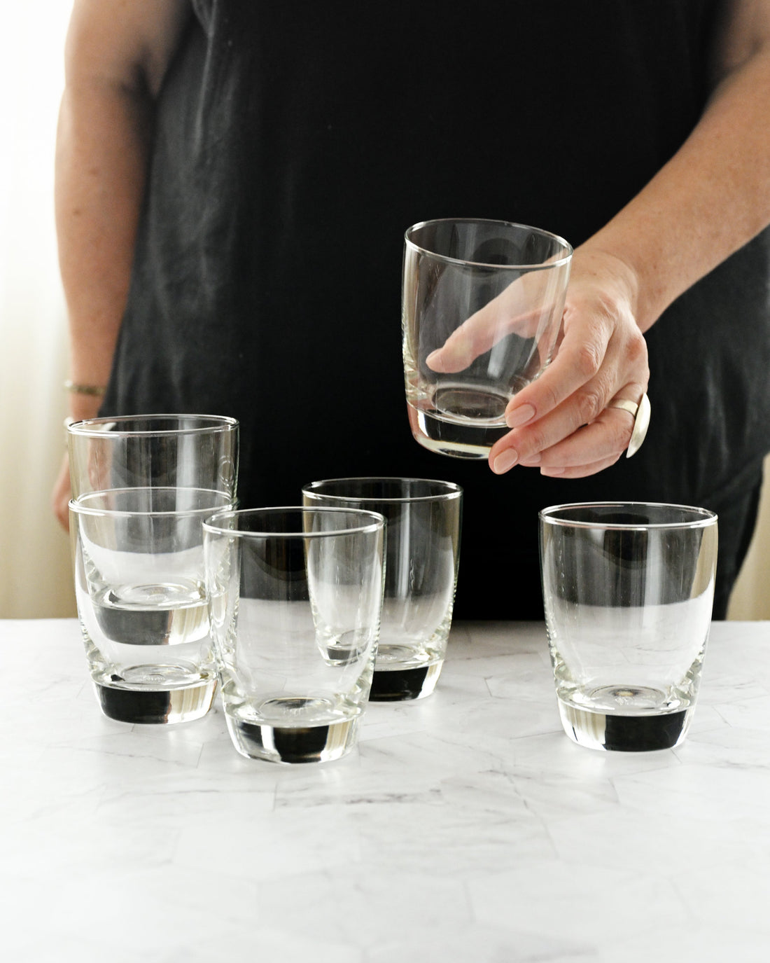 Person holding a clear glass with more glasses on a marble surface