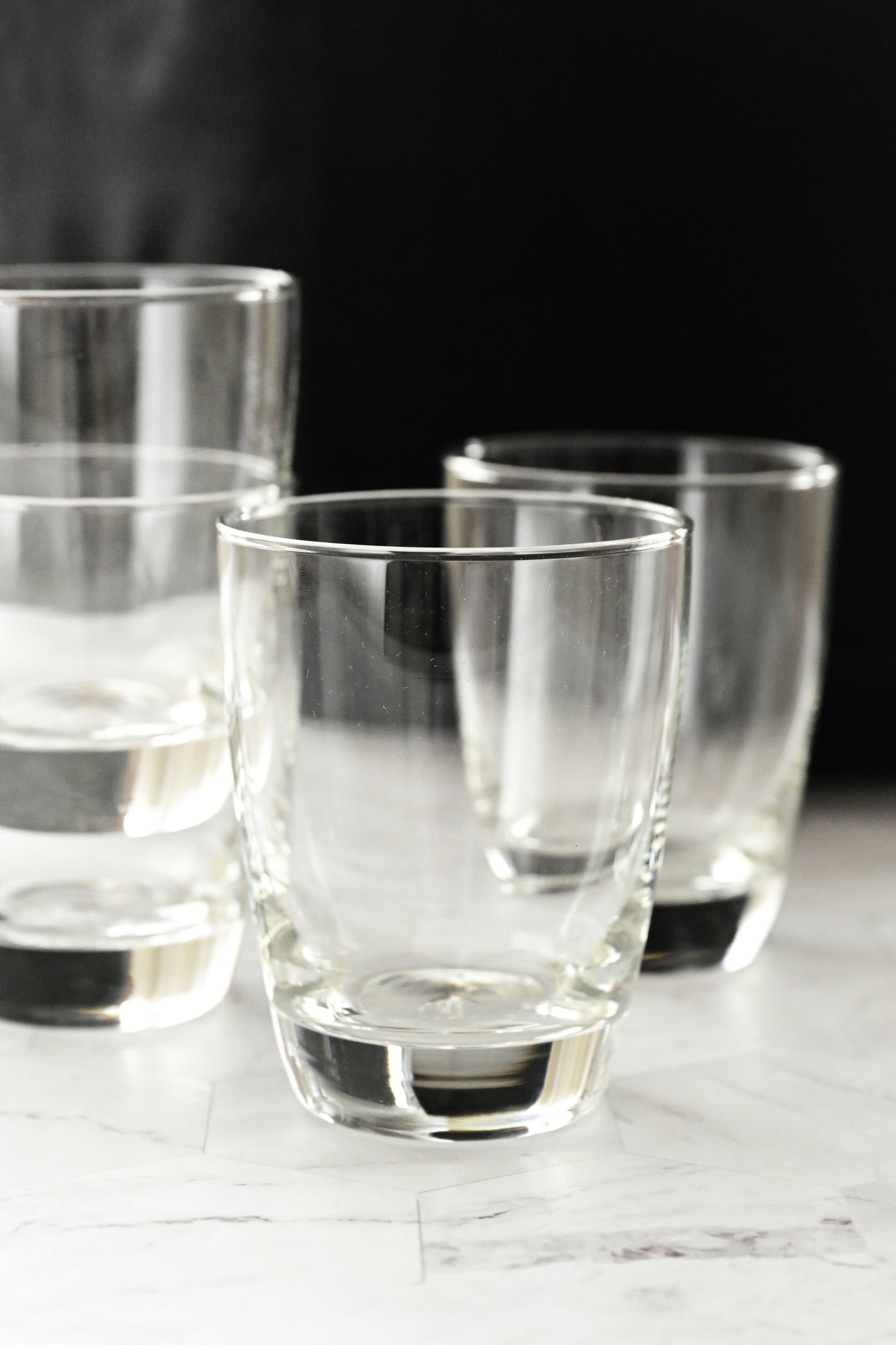 Set of clear glass tumblers on a marble surface with a dark background