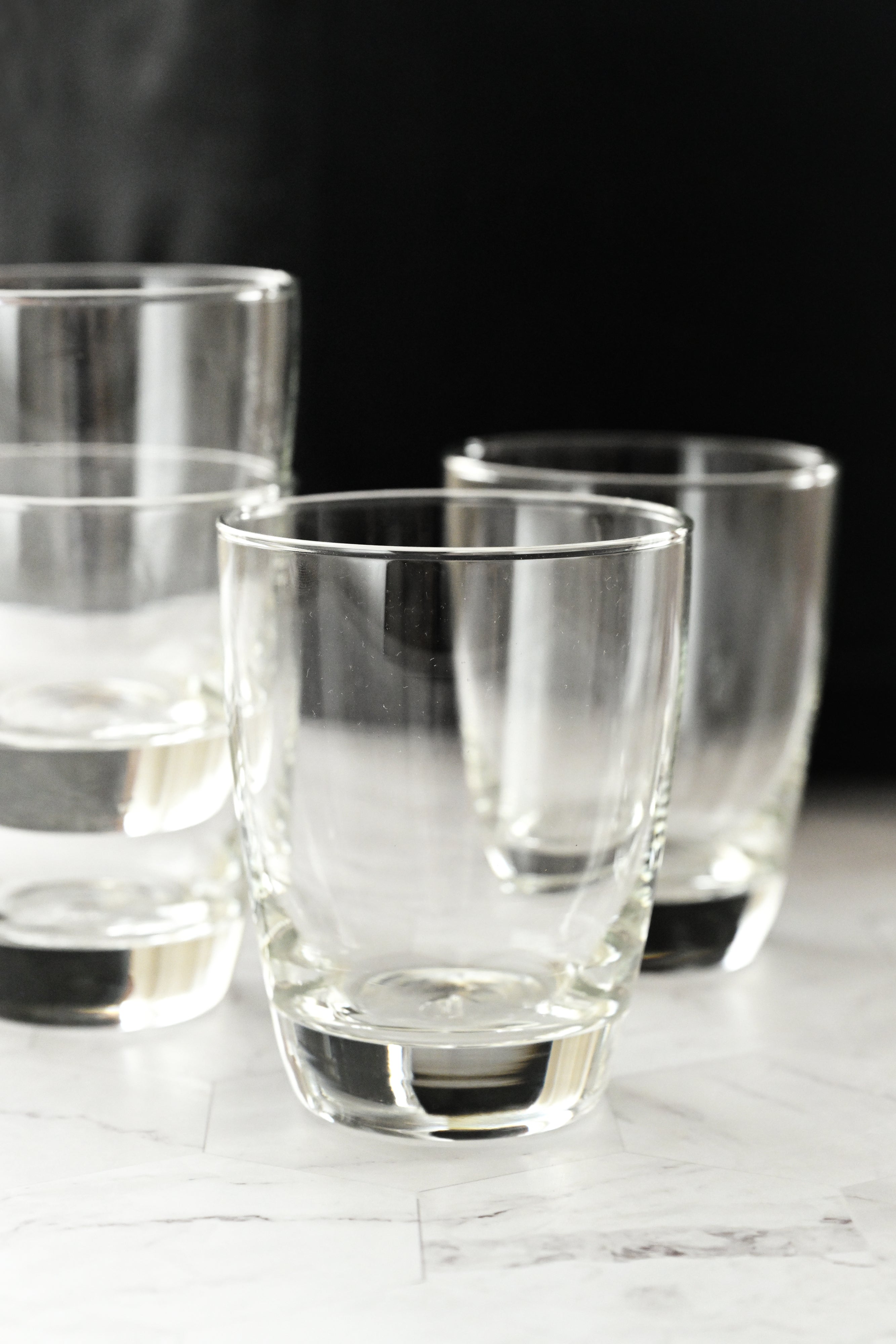 Set of clear glass tumblers on a marble surface with a dark background