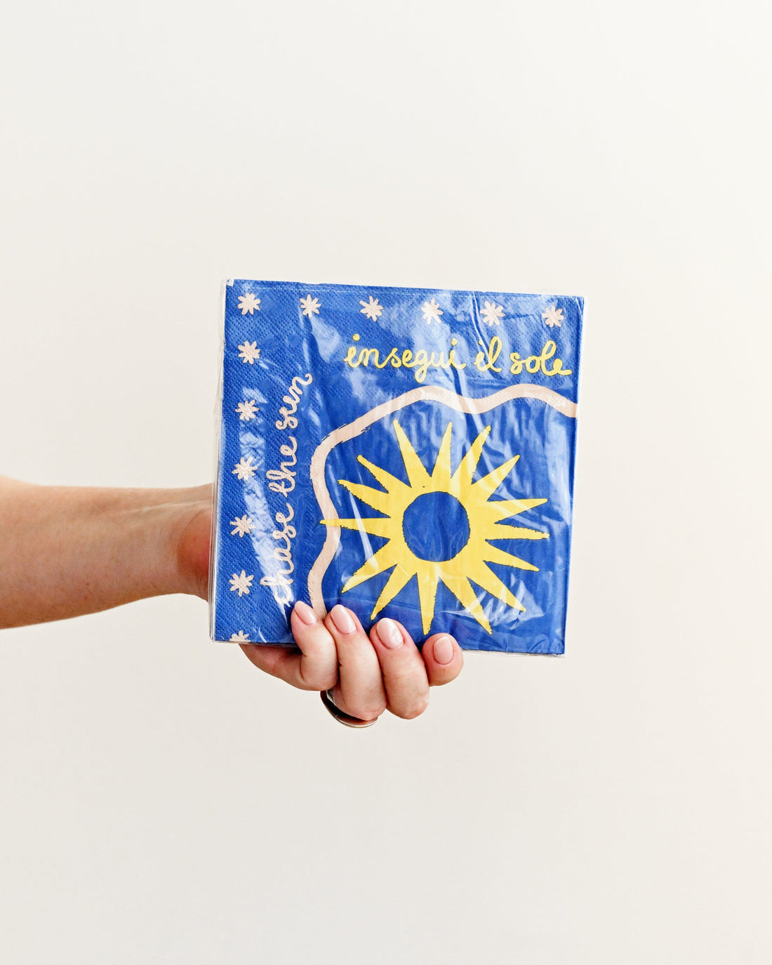 Hand holding a blue package with a sun design on a white background