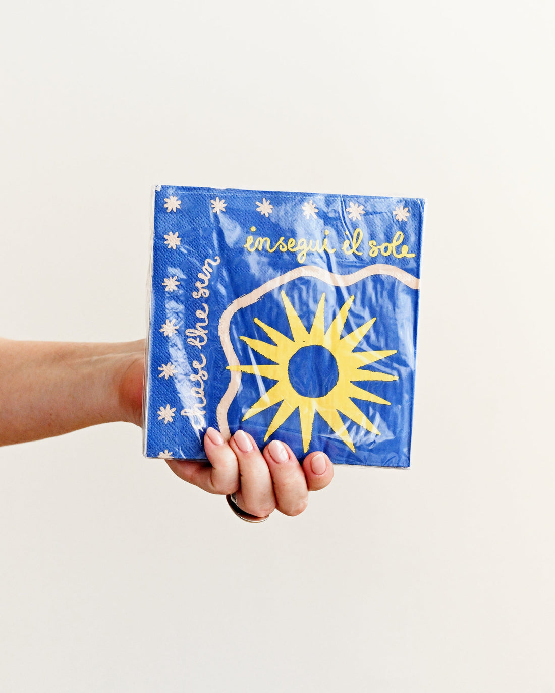 Hand holding a blue package with a sun design on a white background