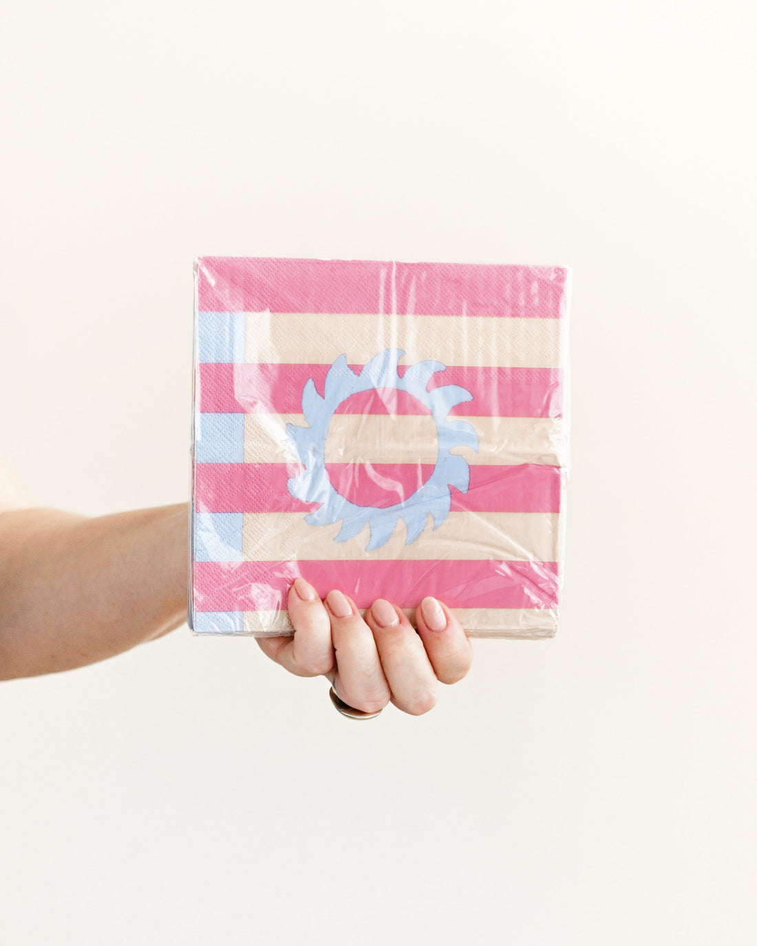 Hand holding a pink and white striped box with a decorative element on a light background