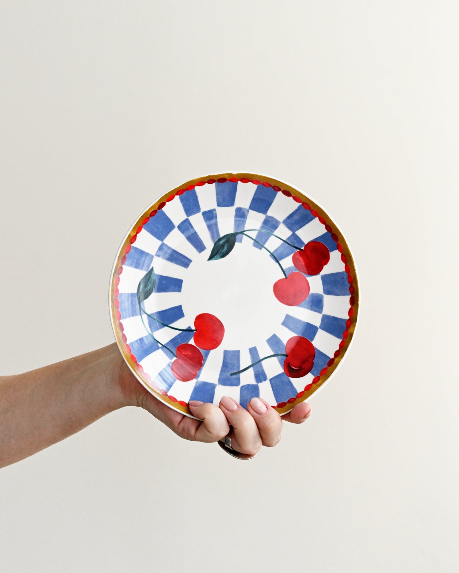 Hand holding a decorative plate with cherry design against a plain background