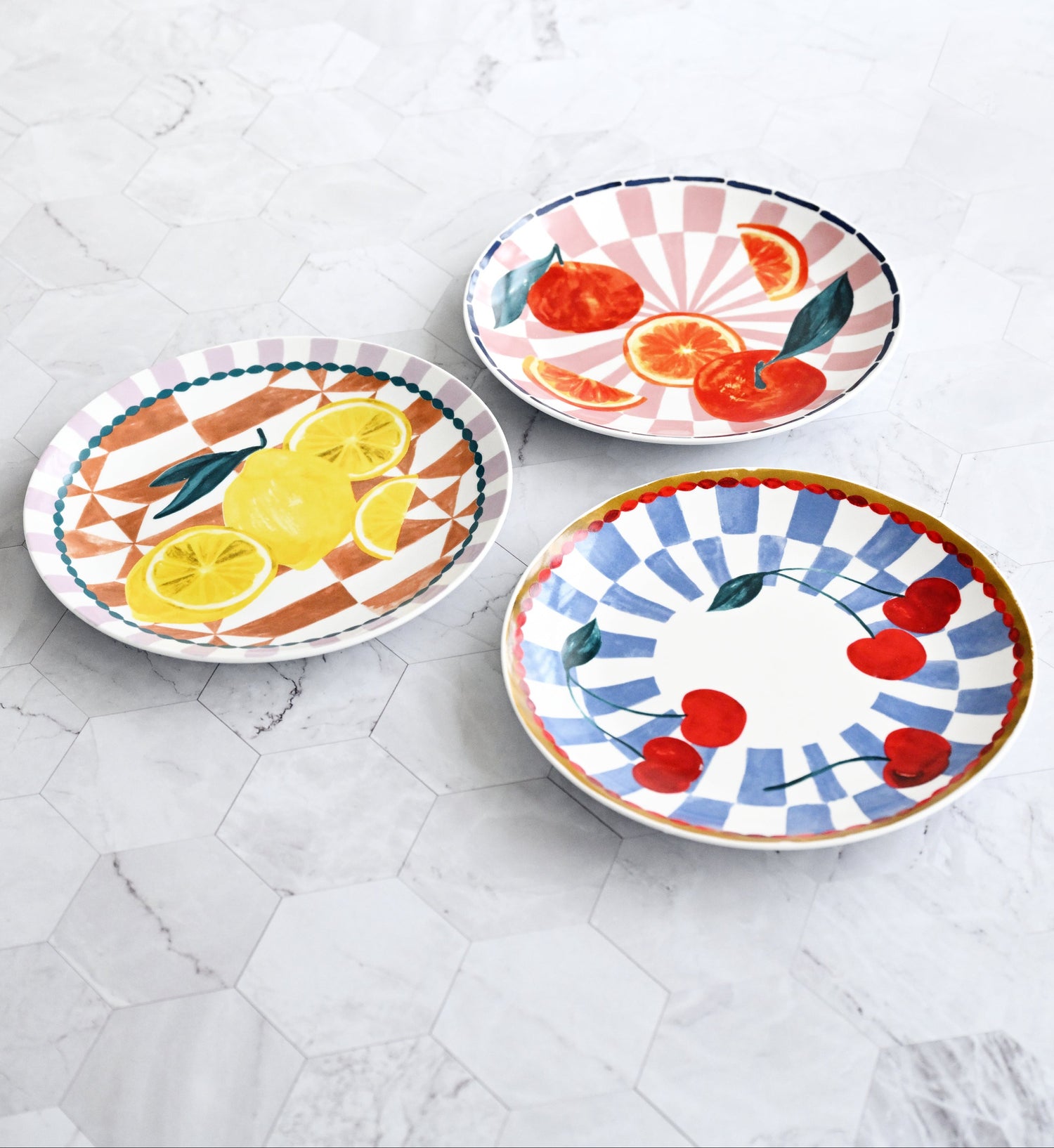 Three colorful ceramic plates with fruit designs on a marble surface.