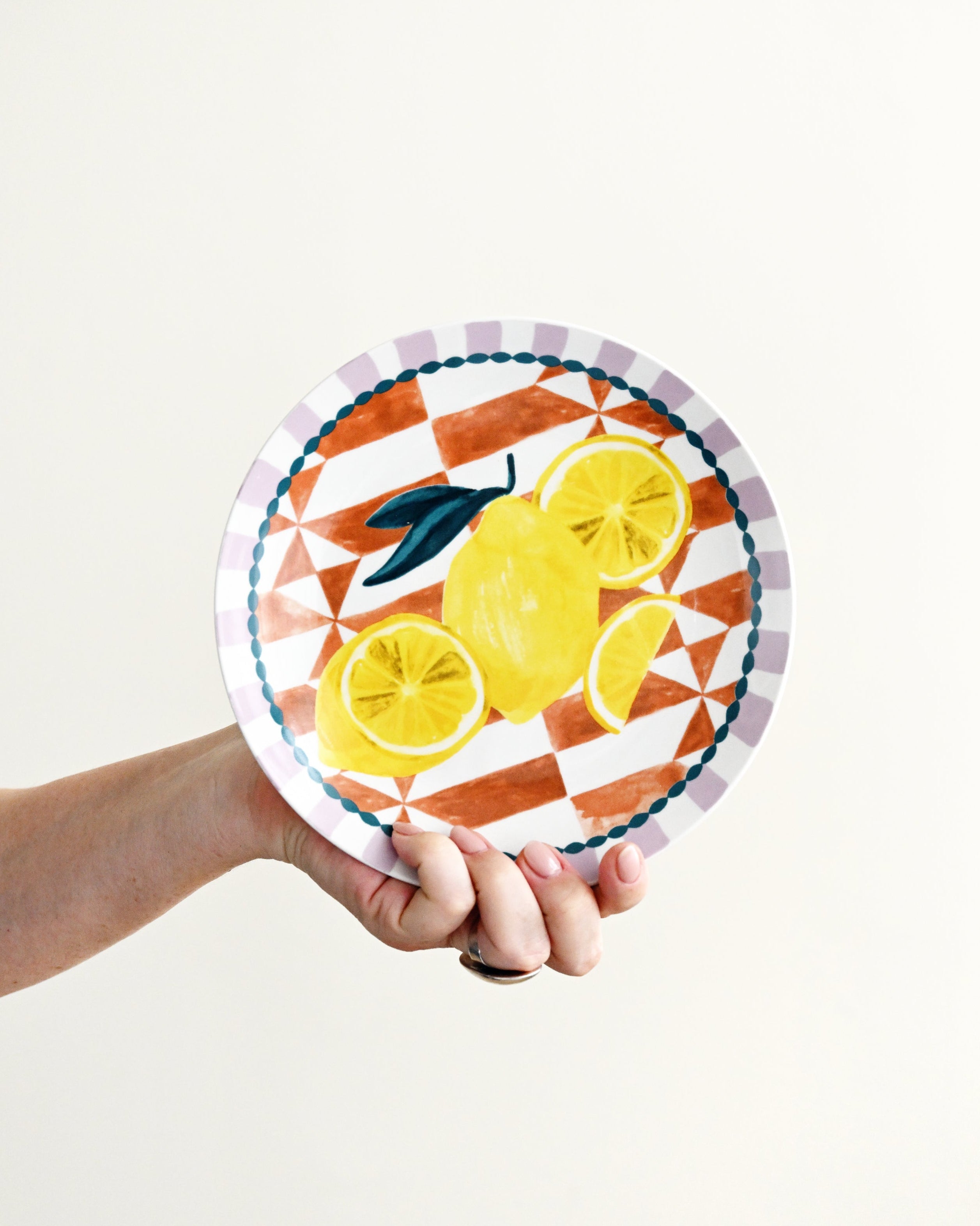 Hand holding a decorative plate with lemon design on a white background