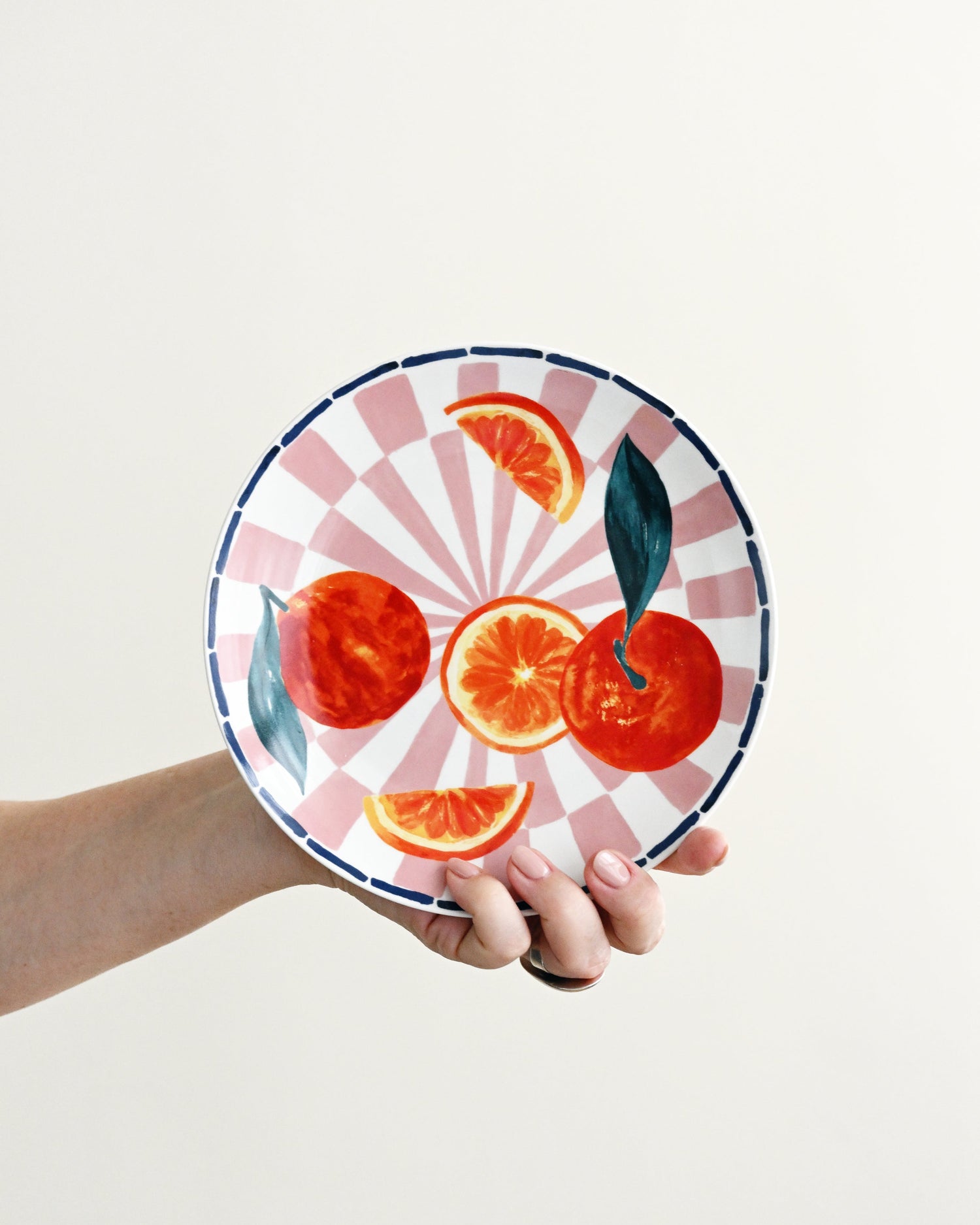 Person holding a decorative plate with orange design on a light background