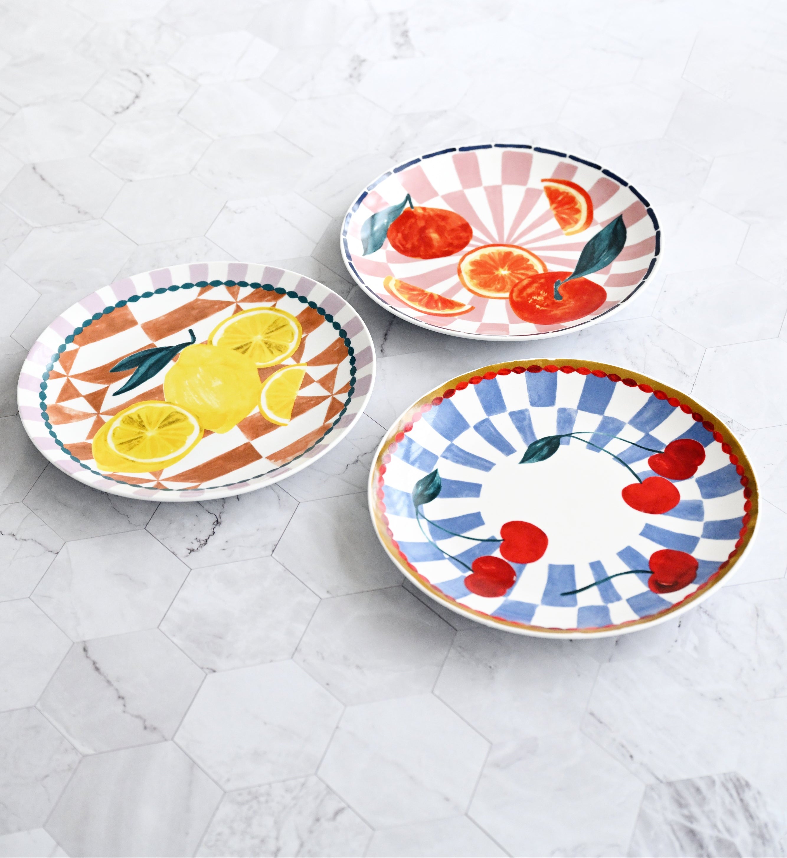 Three colorful ceramic plates with fruit designs on a marble surface.