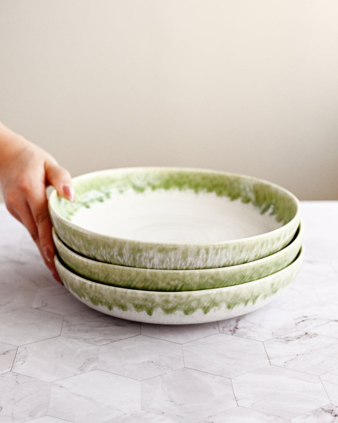 Stack of green-rimmed ceramic bowls held by a hand on a light surface.