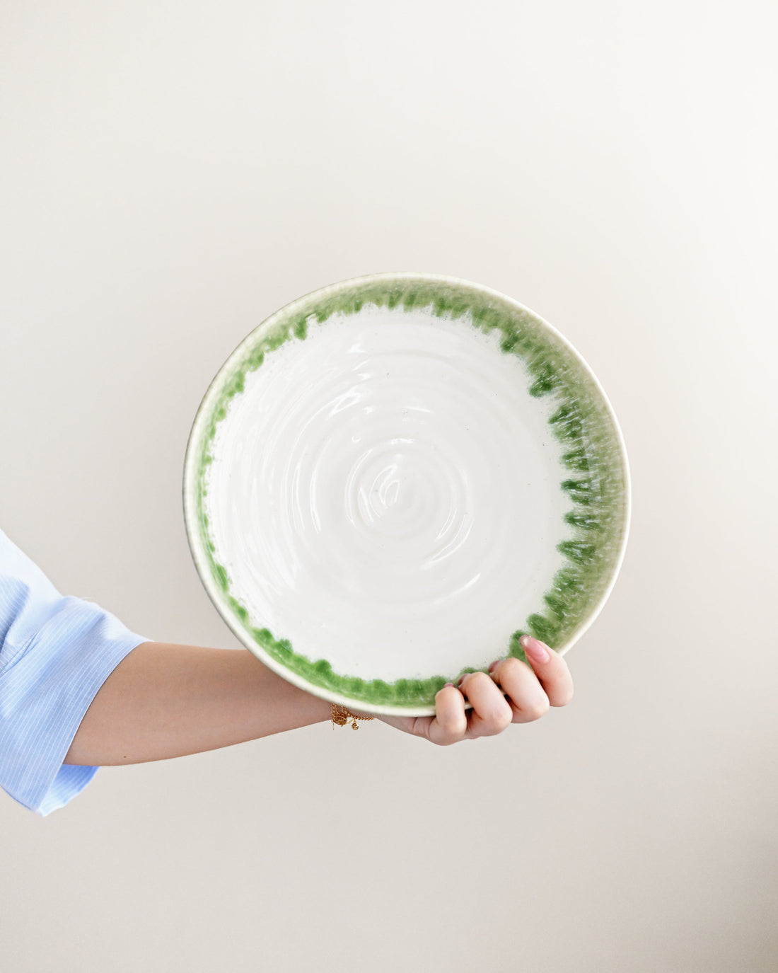 Hand holding a ceramic plate with green rim and pattern on a light background