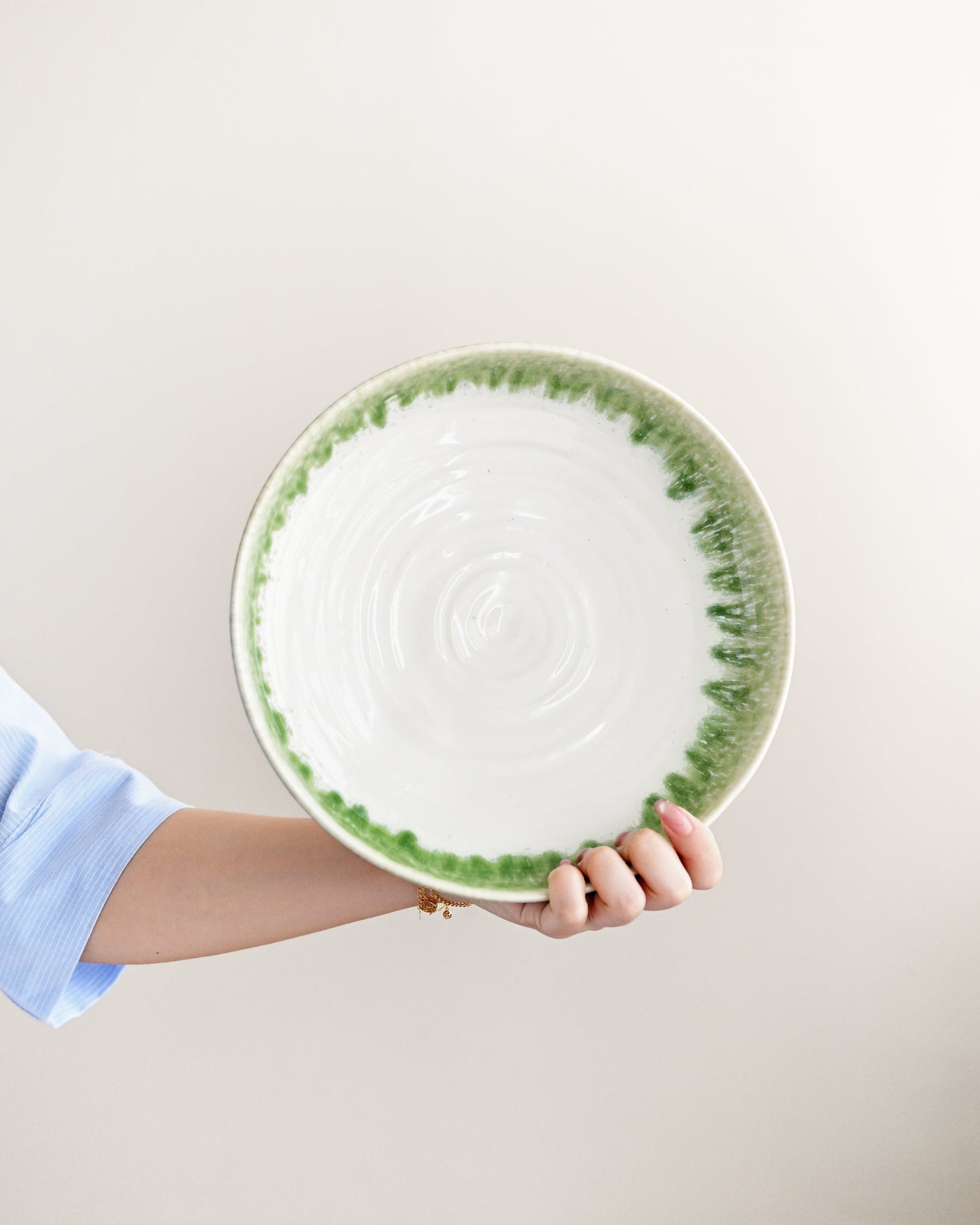 Hand holding a ceramic plate with green rim and pattern on a light background