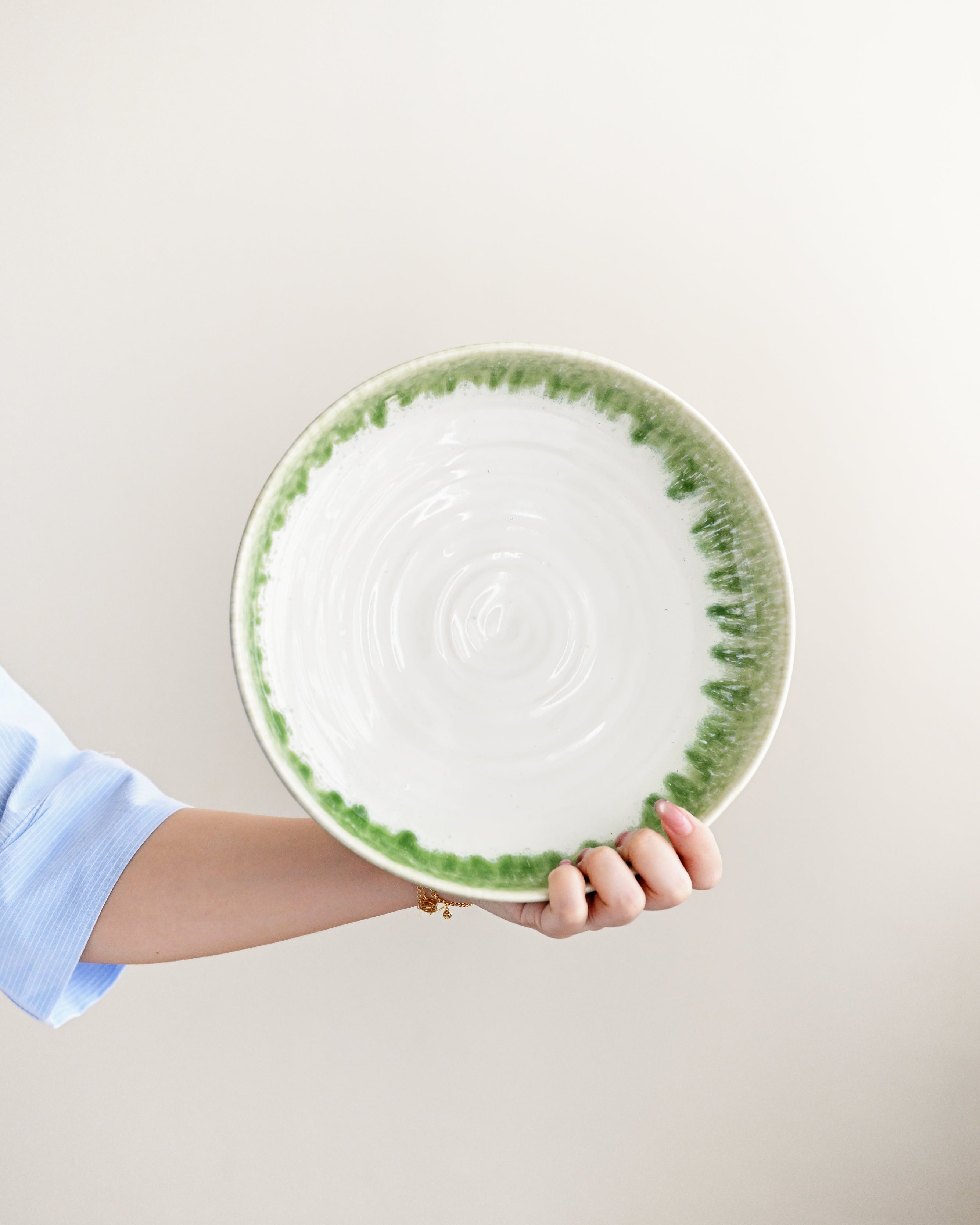 Hand holding a ceramic plate with green rim and pattern on a light background