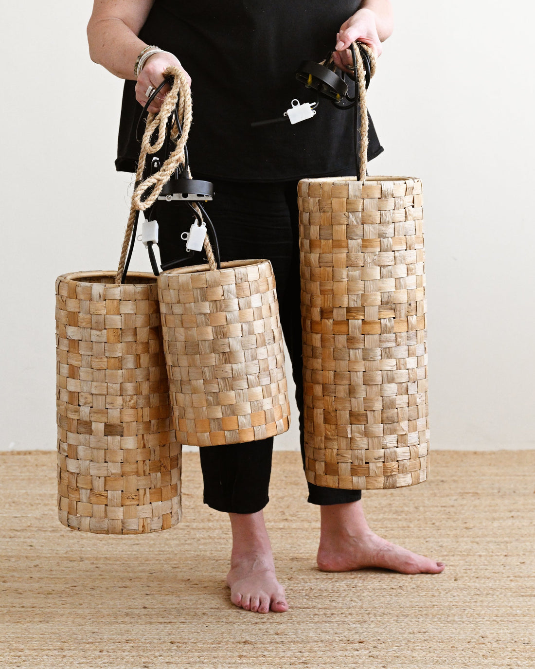 Person holding three woven bags on a wooden floor.