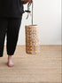 Person holding a woven basket on a wooden floor with a plain background