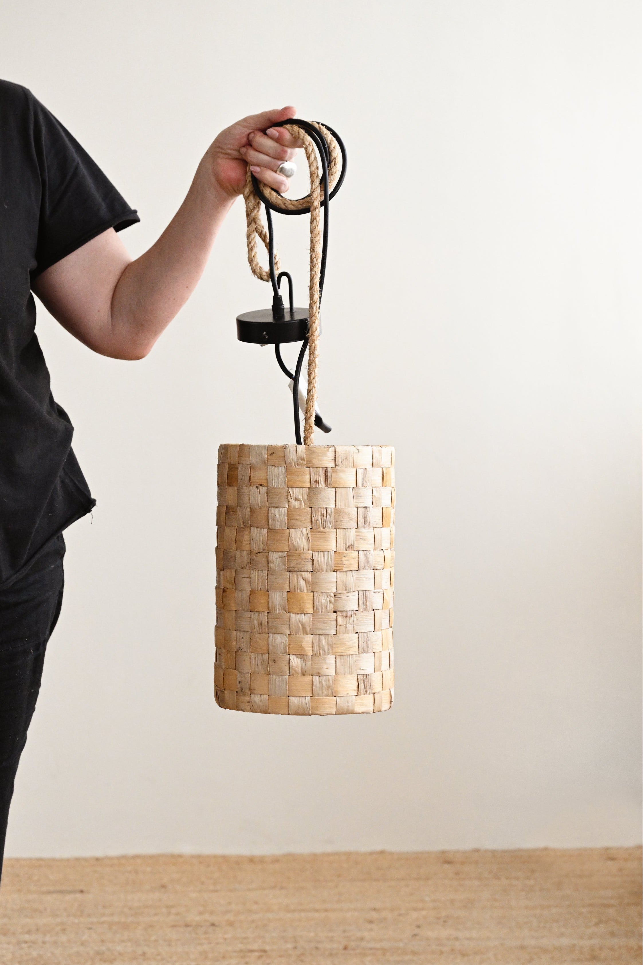 Person holding a woven lampshade against a plain background