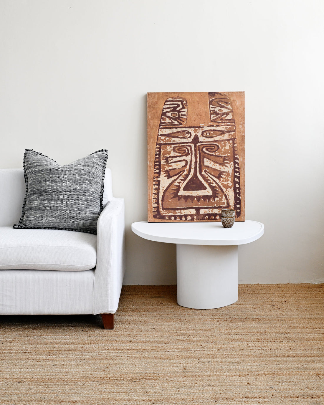 Living room with a white sofa, decorative pillow, and a wooden wall art piece.