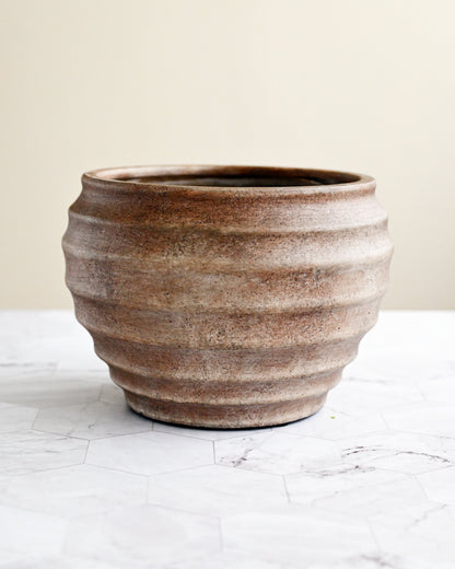 Brown ceramic pot on a white surface with a beige background