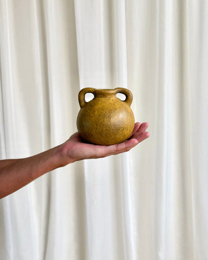 A small round ceramic vessel with two loop handles, held in a person&