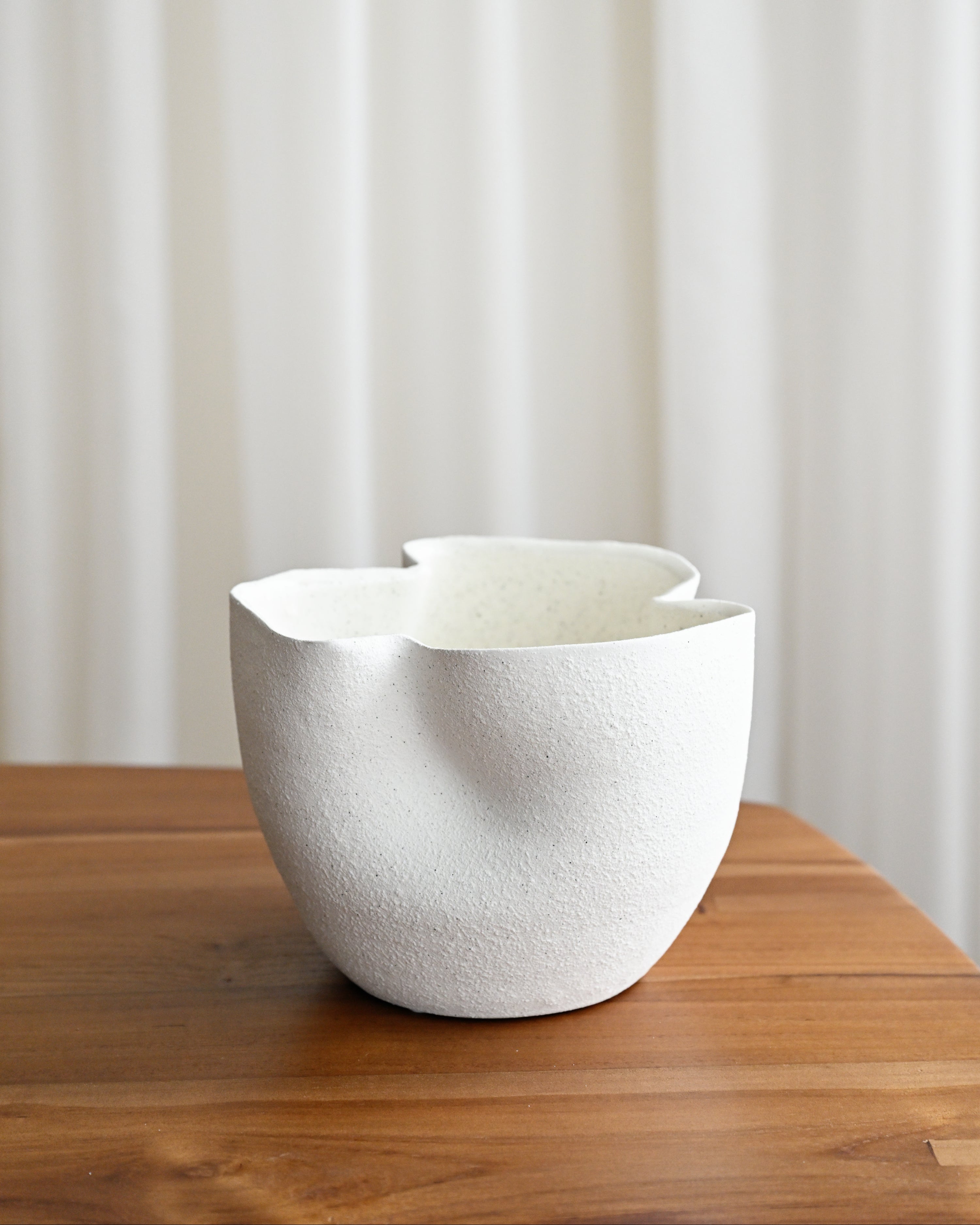 White textured bowl on a wooden surface with a white curtain background