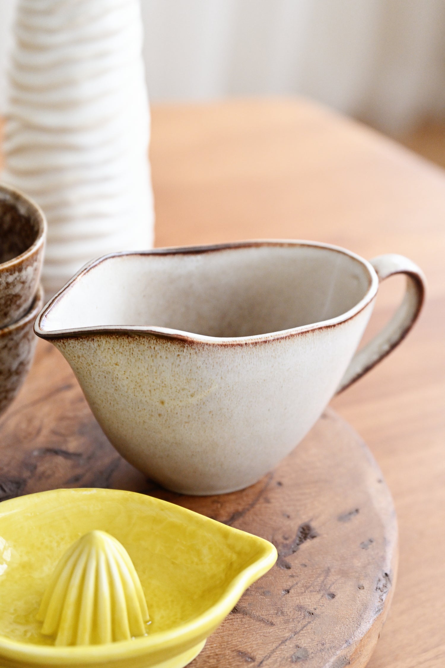 Ceramic pitcher and yellow citrus press on a wooden surface