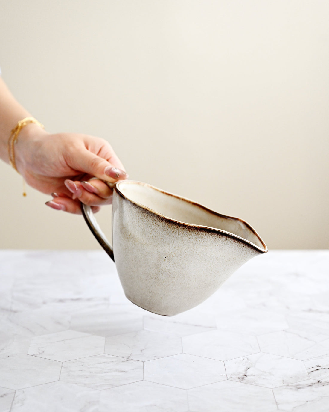 Hand holding a beige fabric bag on a marble surface with a neutral background