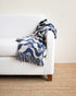 White sofa with a blue and white patterned throw blanket on a beige carpet.