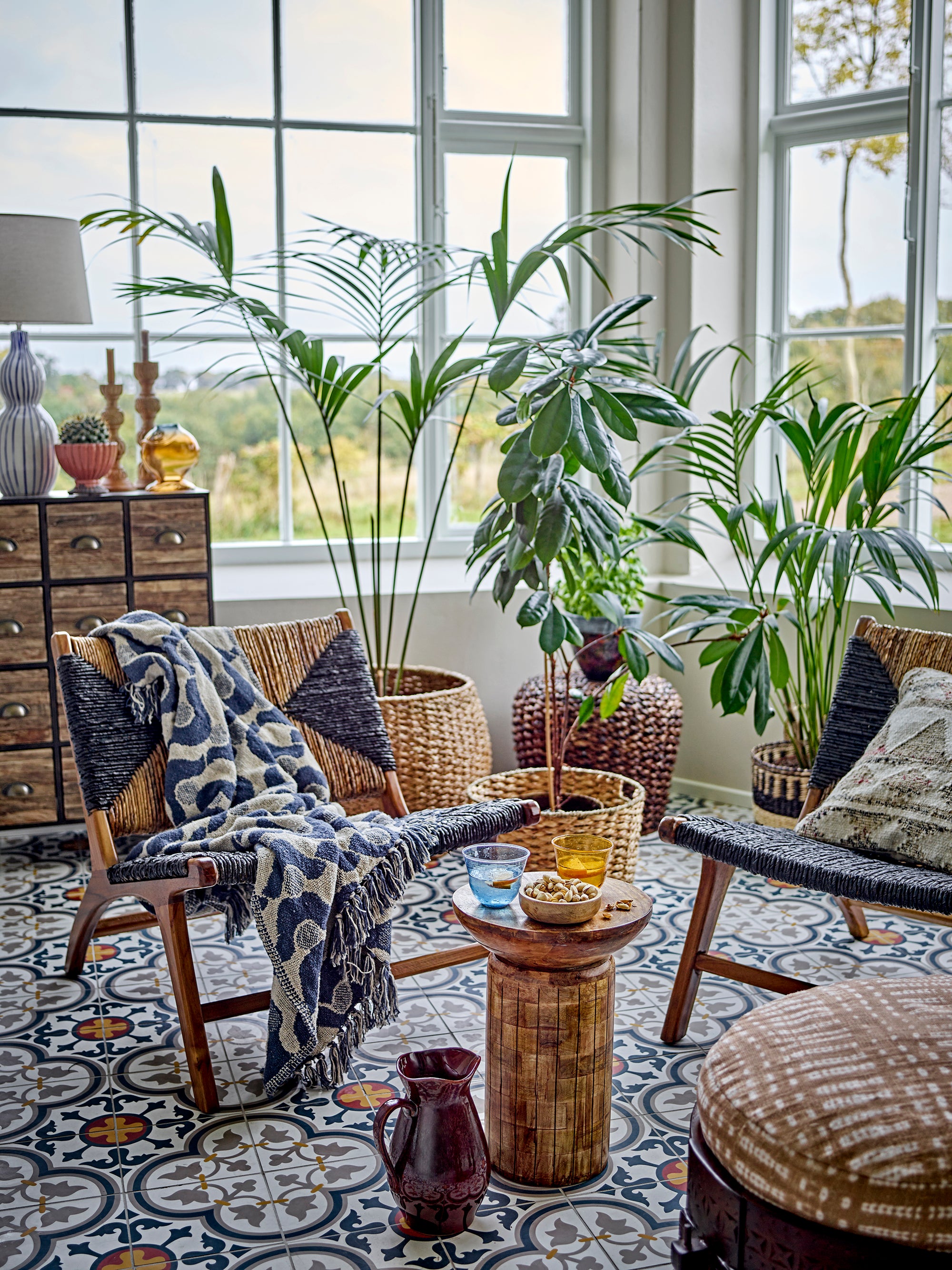 Living room with wicker furniture, plants, and a patterned rug.