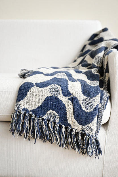 Blue and white patterned throw blanket with tassels on a white couch.
