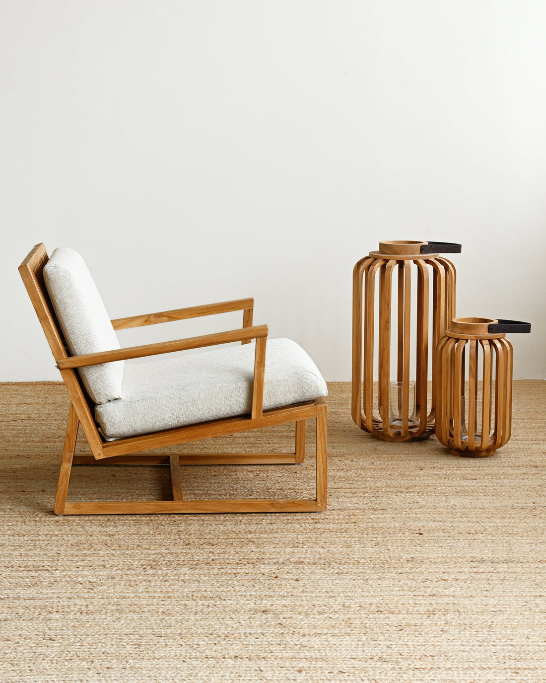Wooden armchair with white cushion and two bamboo vases on a wooden floor.