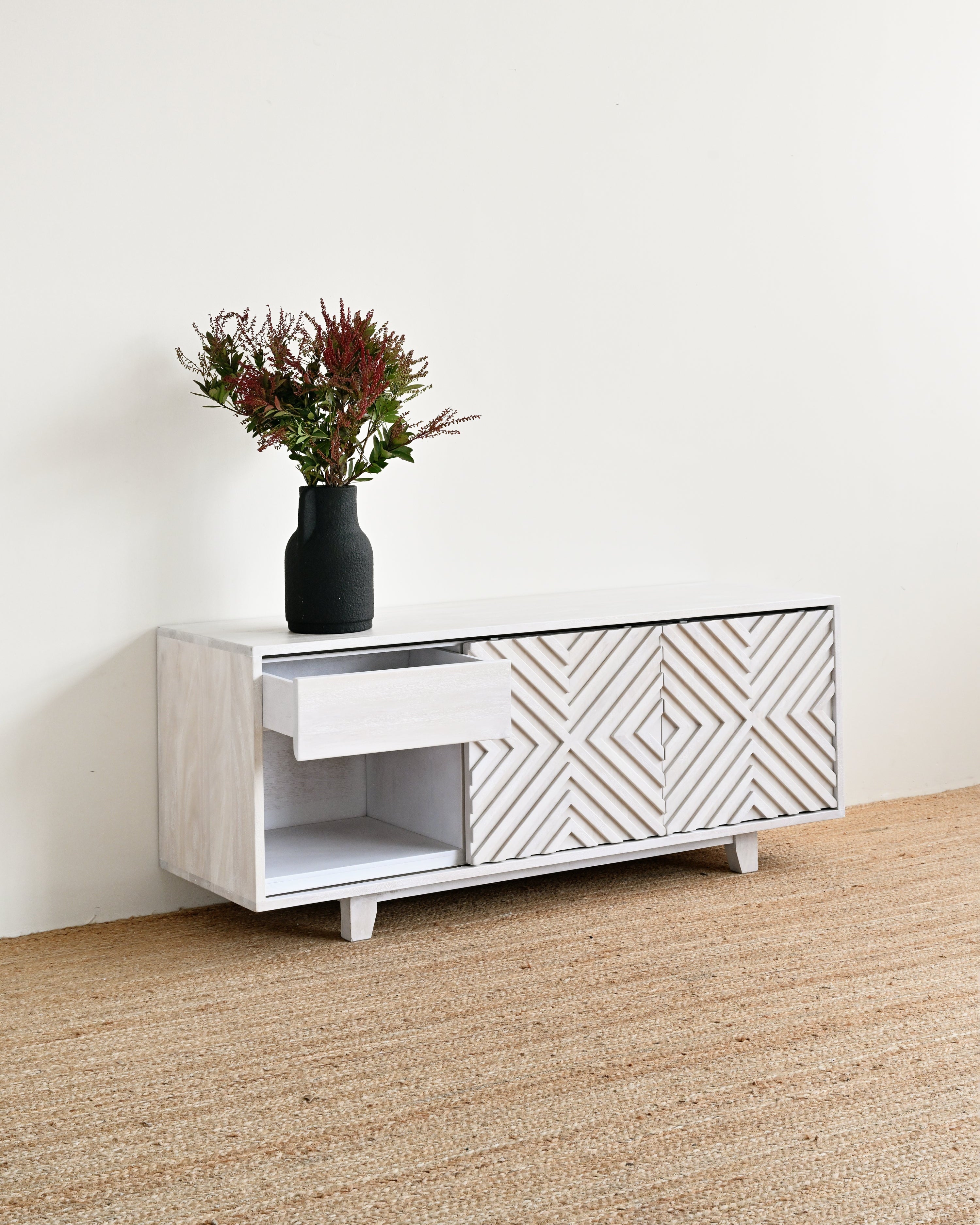 White and gray patterned sideboard with a vase of flowers on a wooden floor.