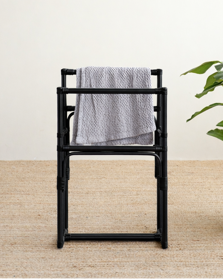 Black bamboo chair with a gray towel draped over it on a light wooden floor.