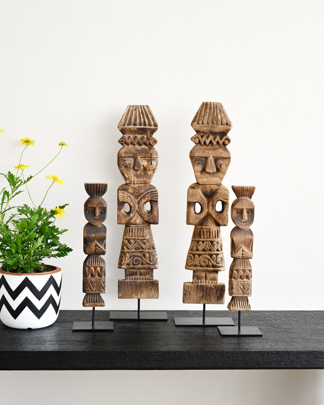 Three wooden tribal figurines on stands with a plant in the background