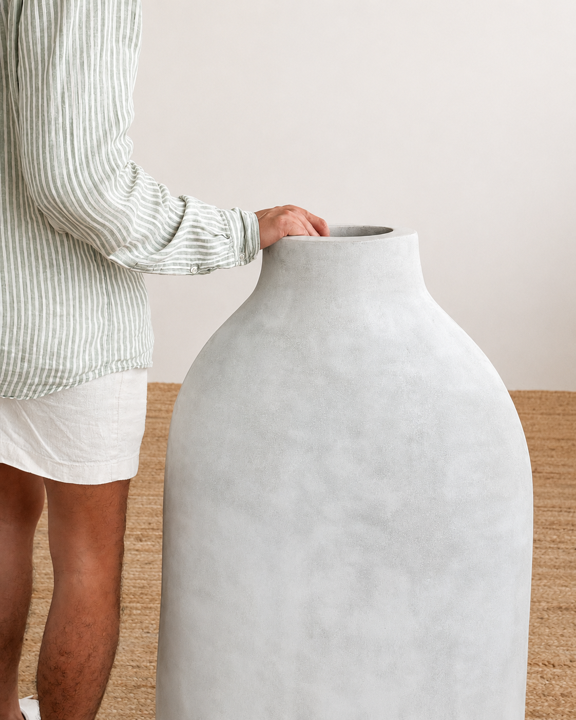Person holding a large gray ceramic vase against a neutral background