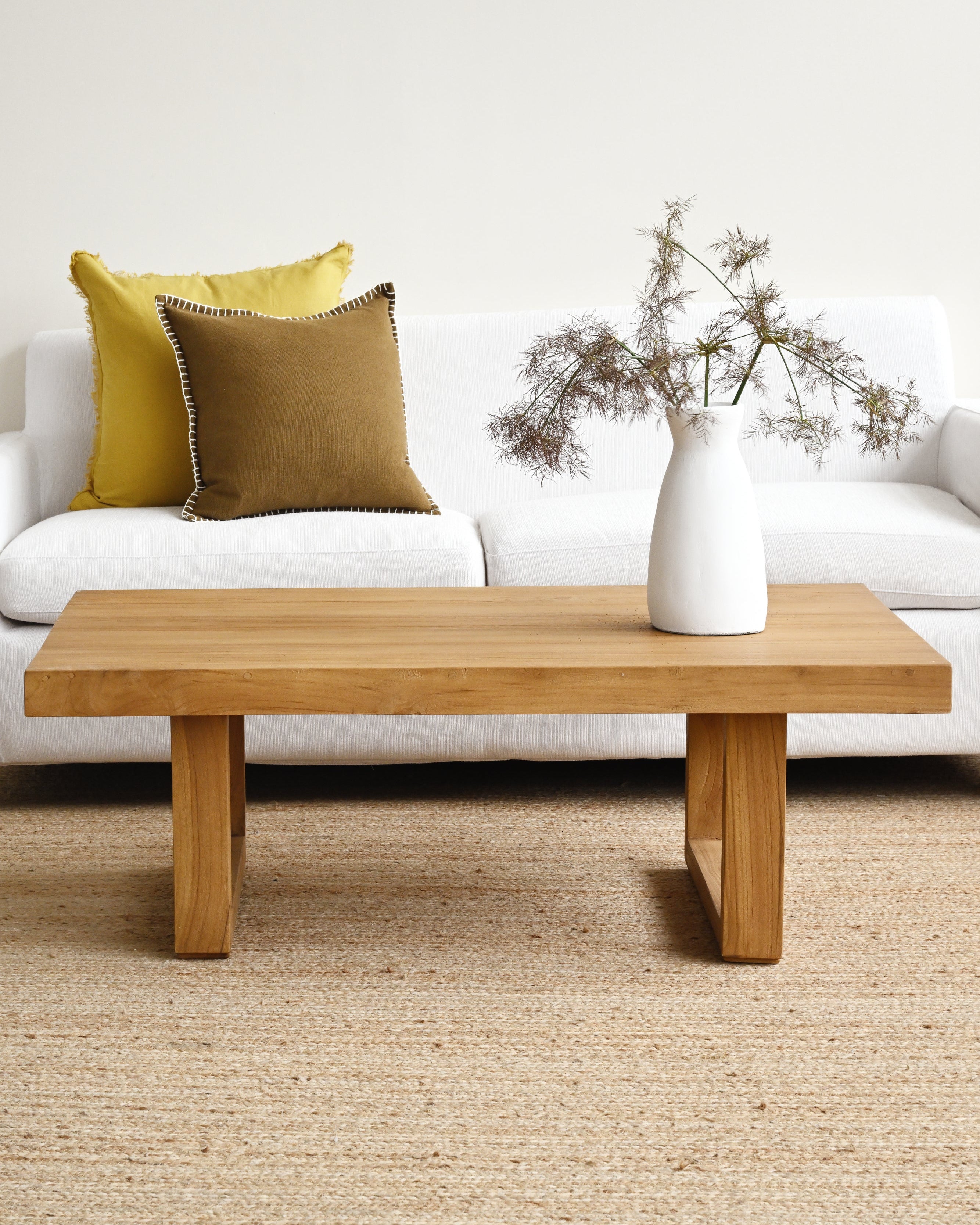 Wooden coffee table with a vase and decorative plant in a living room setting.