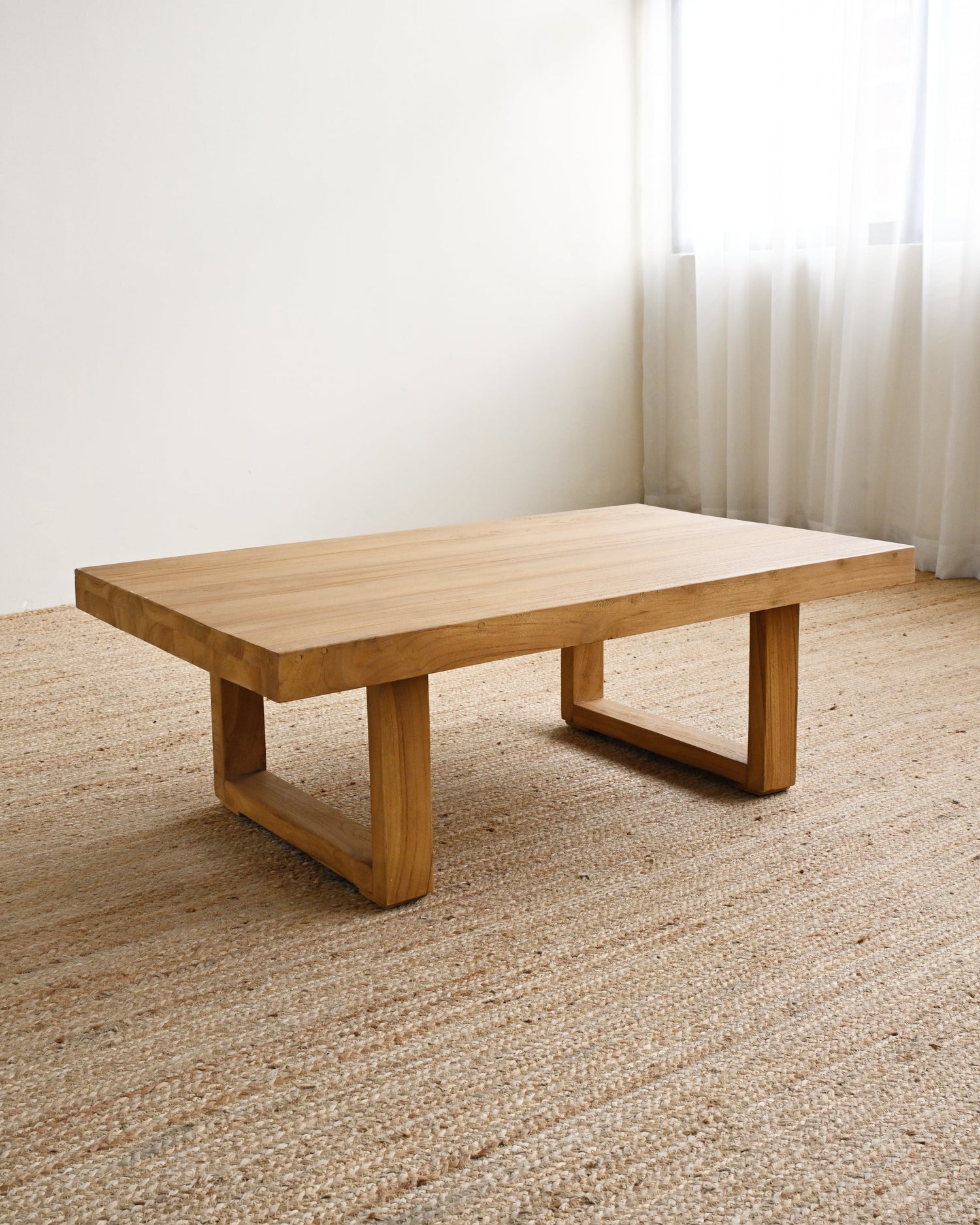 Wooden coffee table in a room with light-colored carpet and sheer curtains.