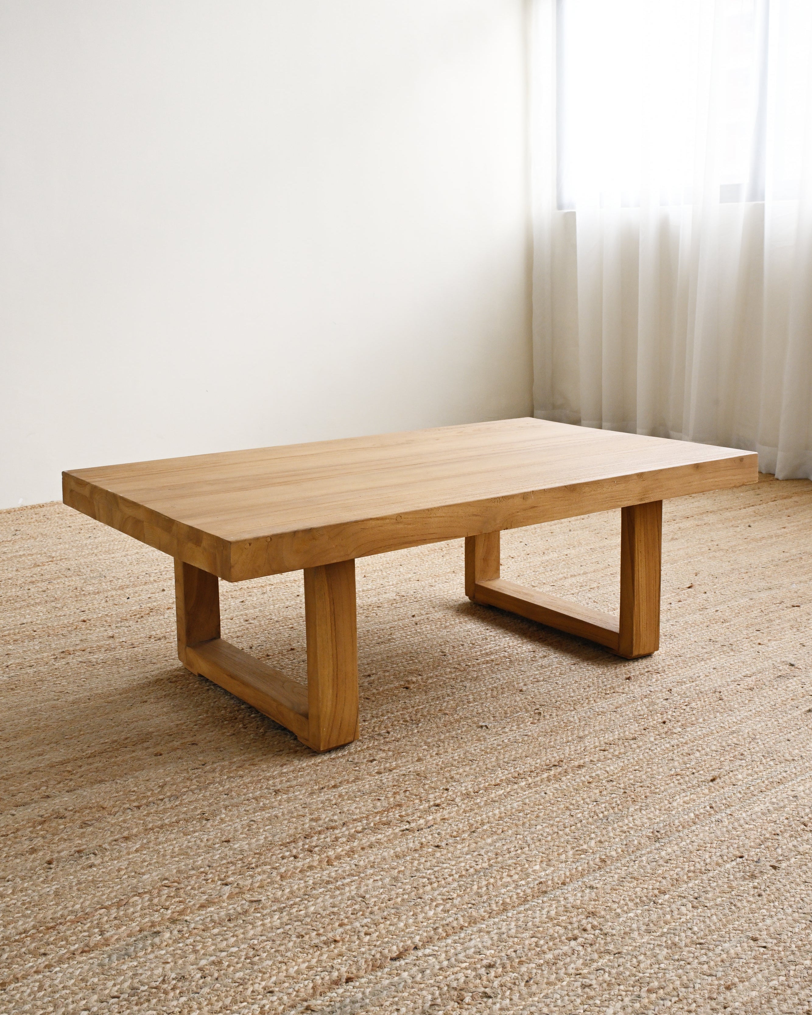 Wooden coffee table in a room with light-colored carpet and sheer curtains.
