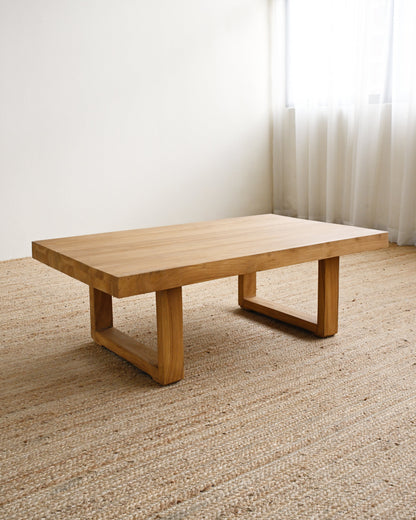 Wooden coffee table in a room with light-colored carpet and sheer curtains.