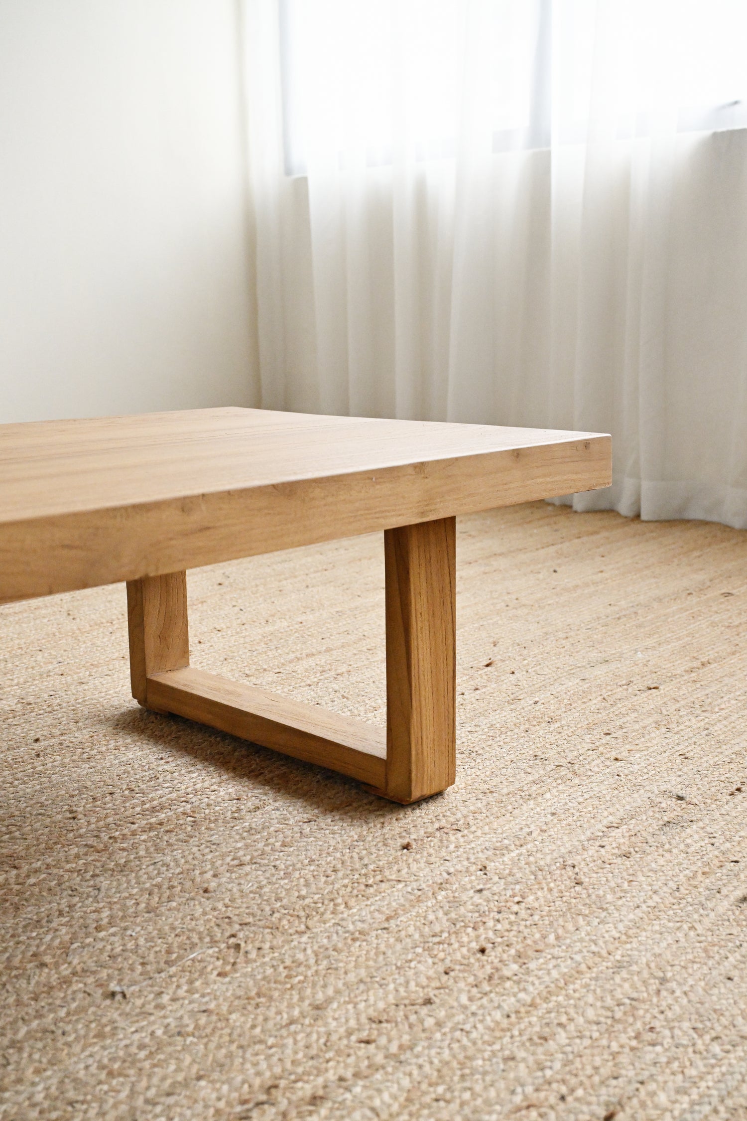 Wooden coffee table on a beige carpet with white curtains in the background