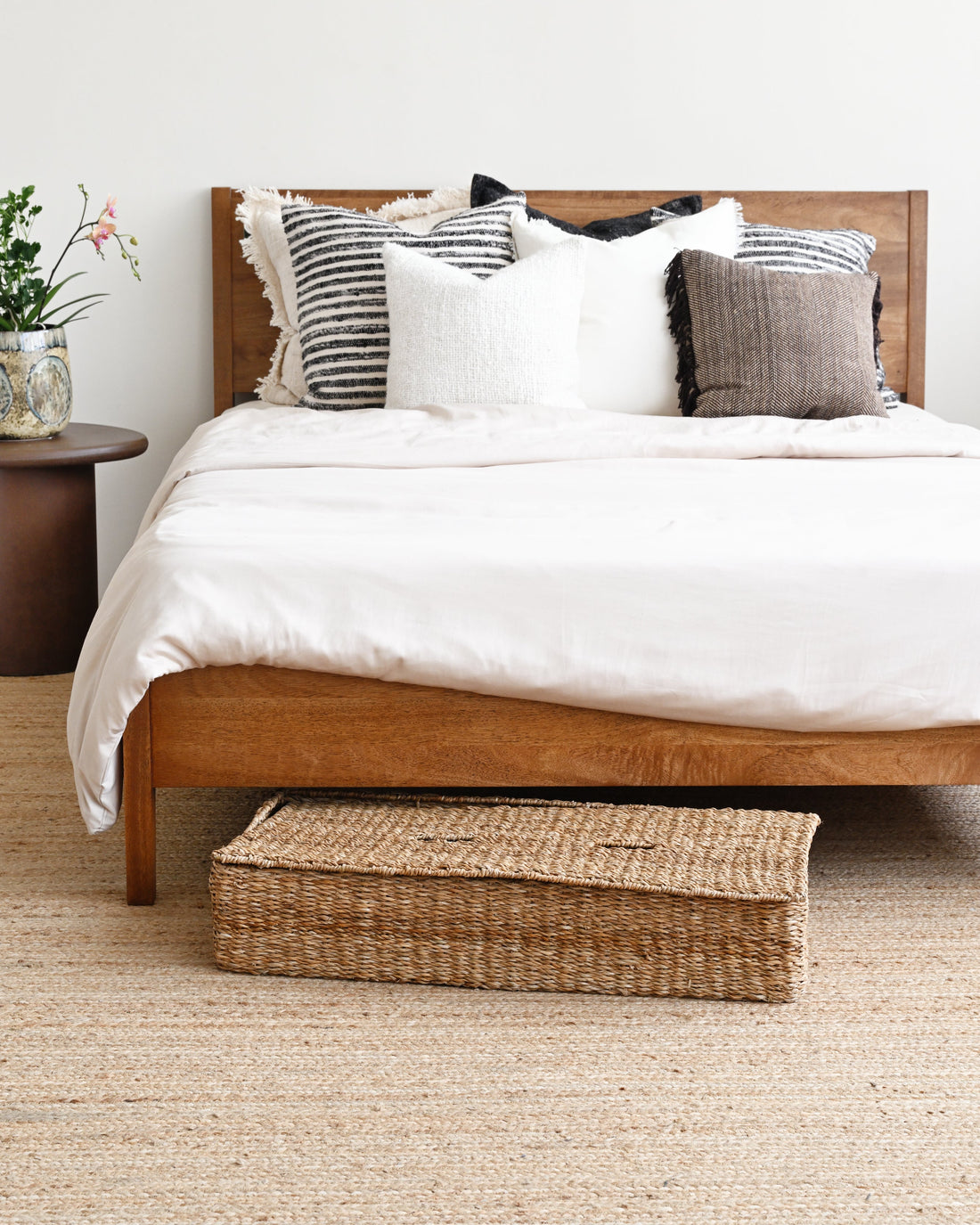 Bedroom with wooden bed, white bedding, and a woven basket on a beige carpet.