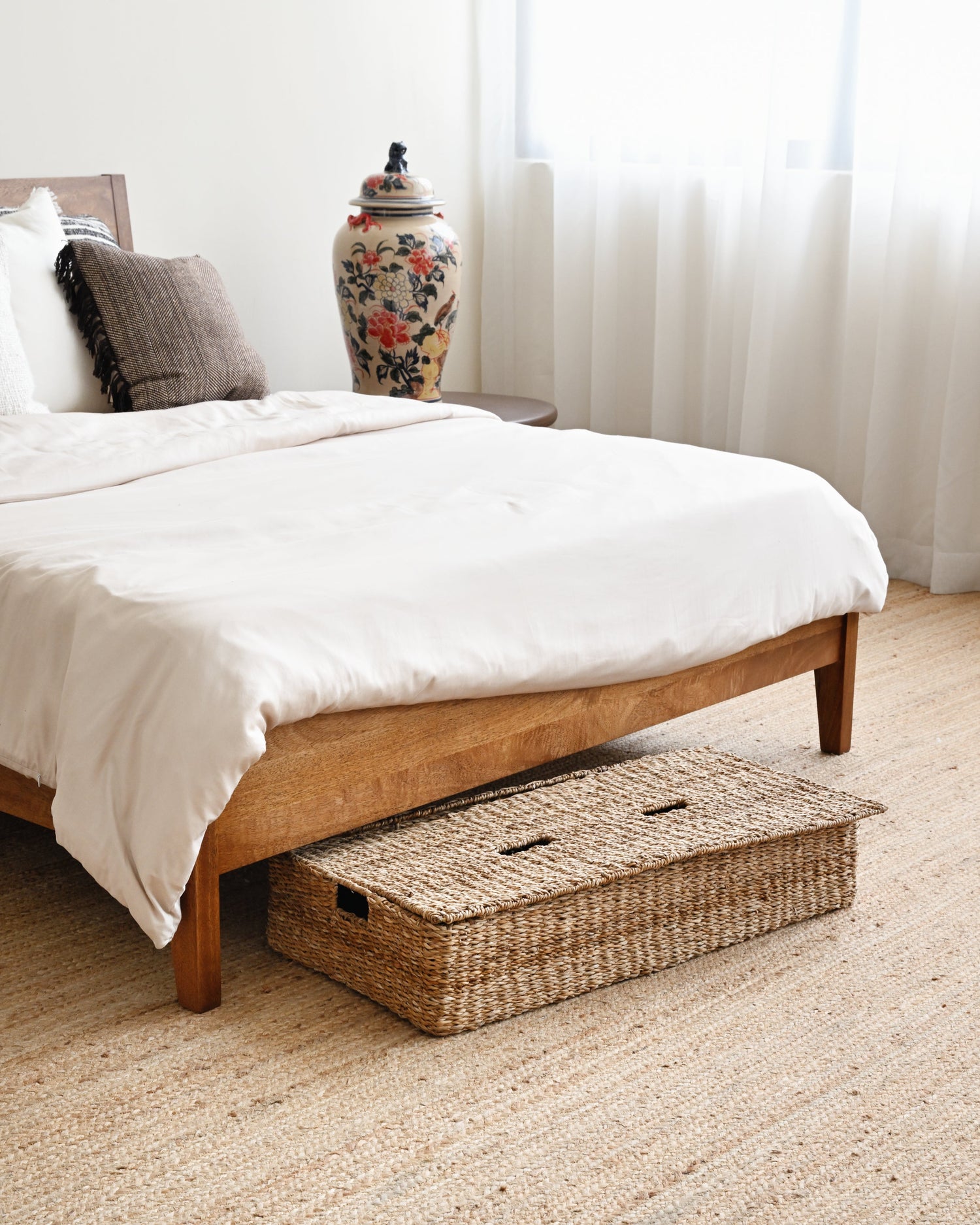 Wooden bed with white bedding and a woven basket at the foot of the bed in a bedroom setting.