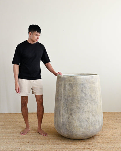 Man holding a large concrete planter indoors with a plain background