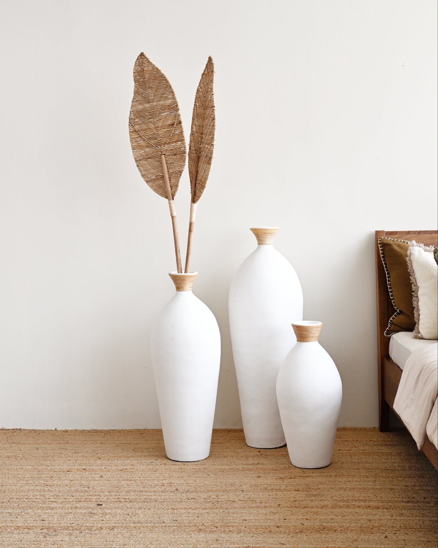 Three white vases with gold accents on a wooden floor against a white wall.