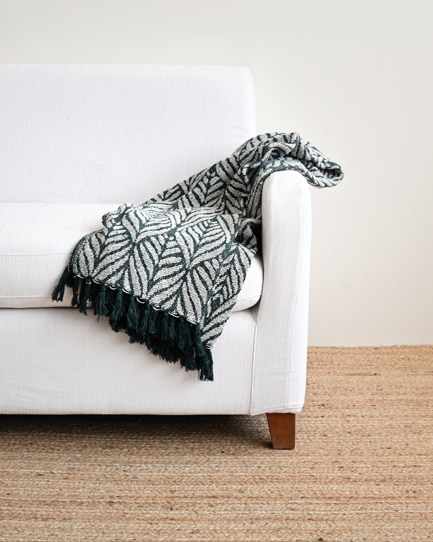 White couch with a patterned green and black blanket draped over it on a beige carpet.