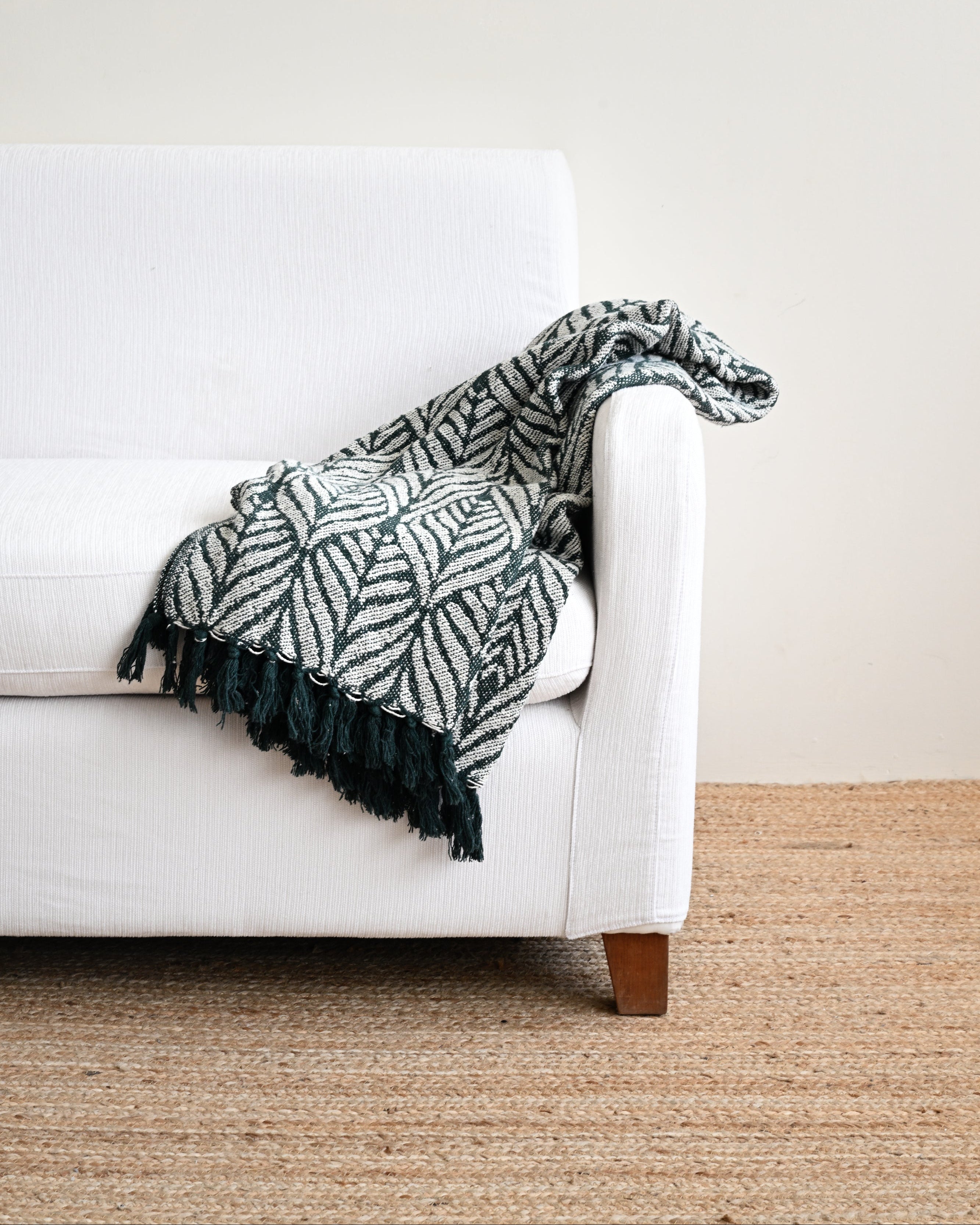 White couch with a patterned green and black blanket draped over it on a beige carpet.
