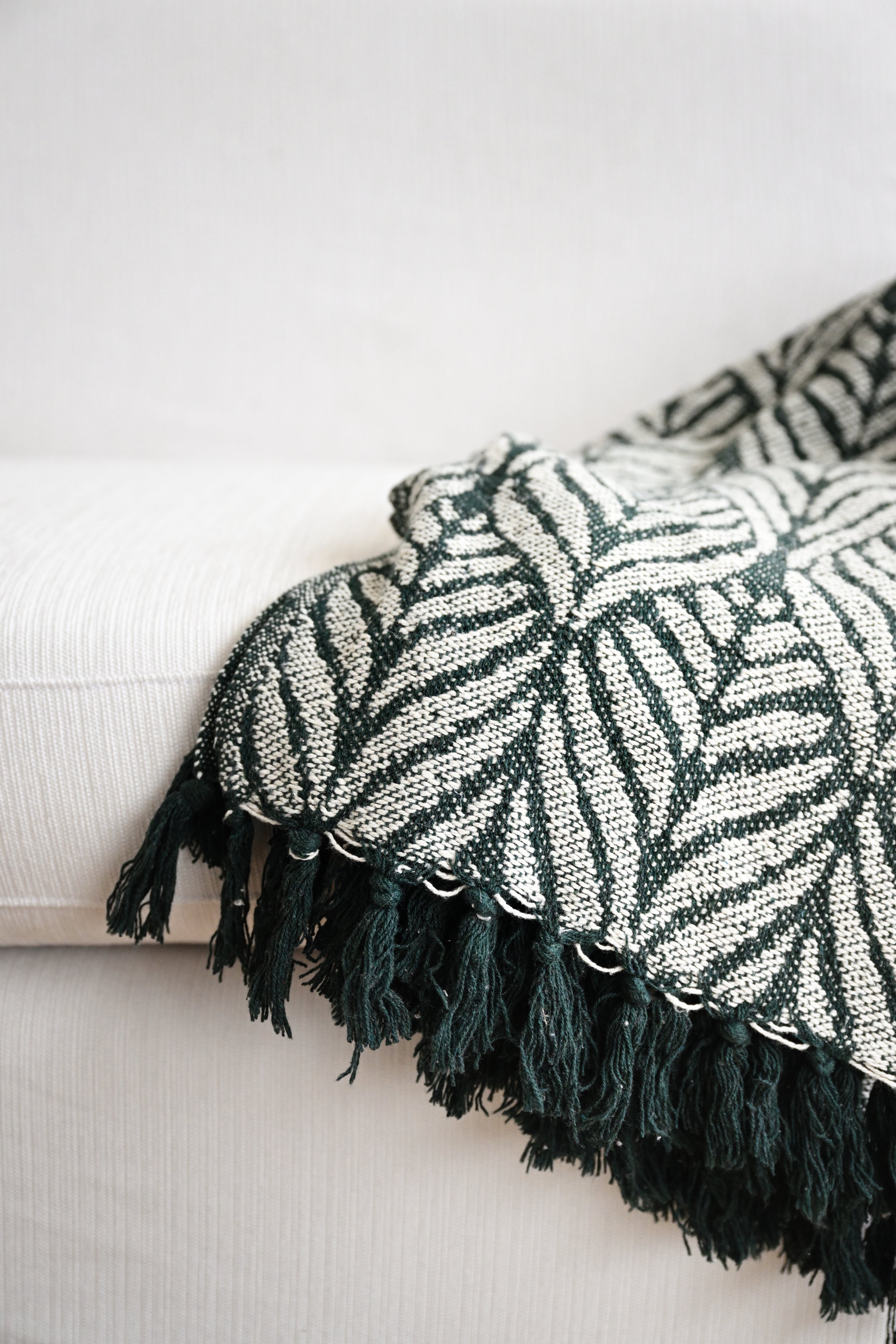 Green and white patterned throw blanket with tassels on a light-colored sofa.