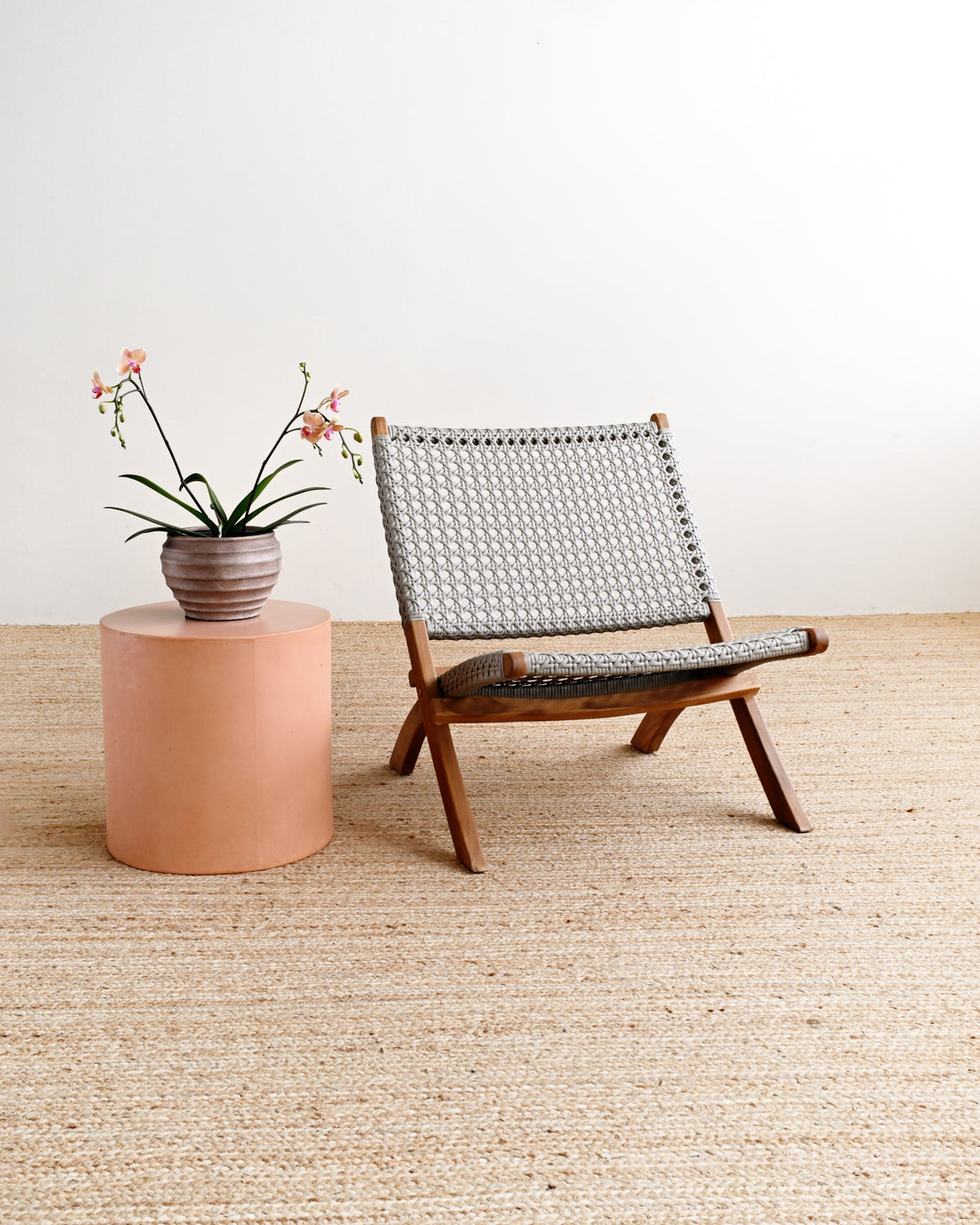 Wooden chair with woven backrest next to a small round table with a plant on a beige carpet.