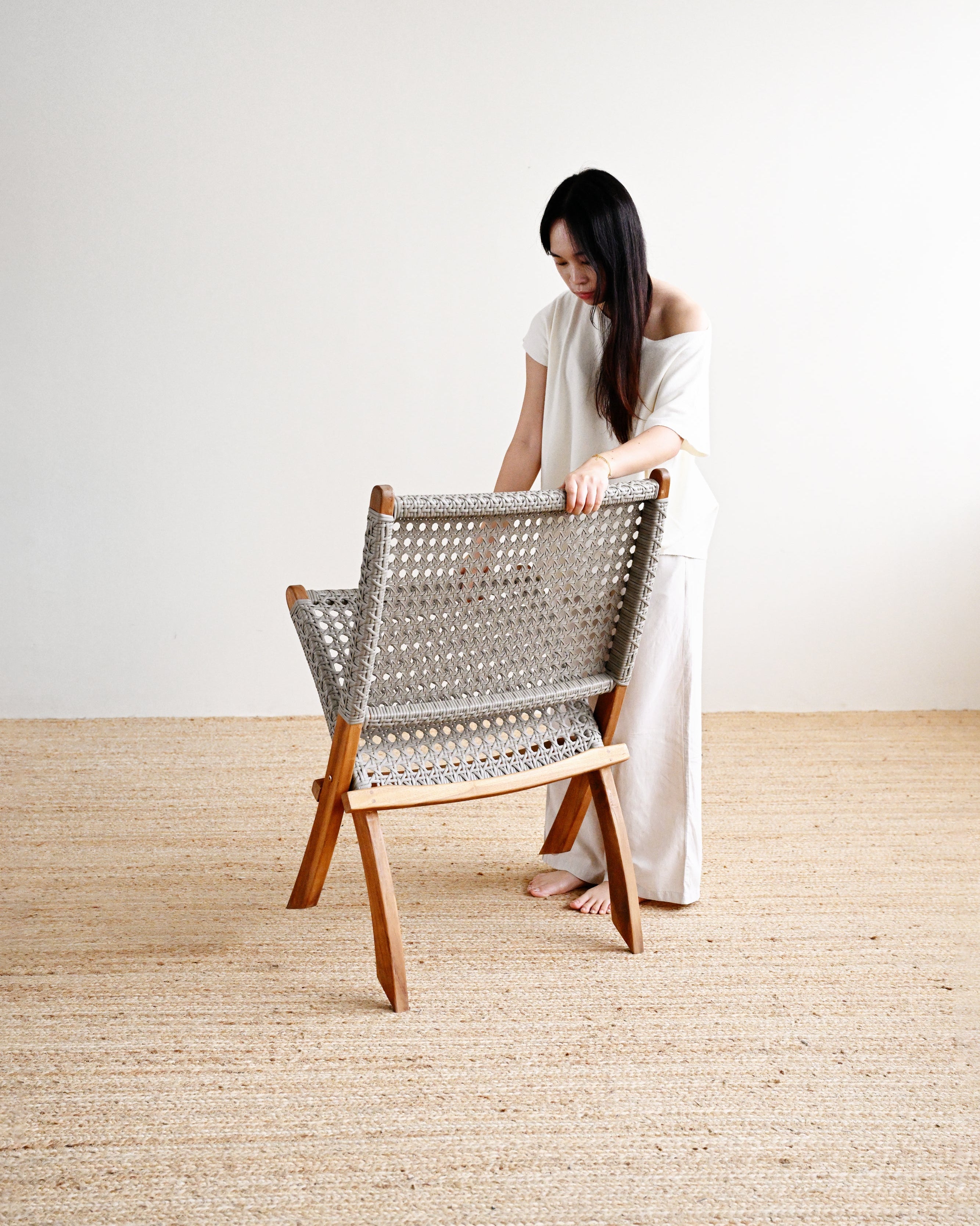 Woman in a white dress standing next to a wooden chair with a woven backrest on a beige carpet.