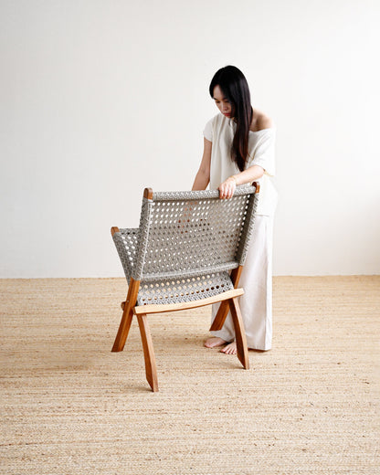 Woman in a white dress standing next to a wooden chair with a woven backrest on a beige carpet.