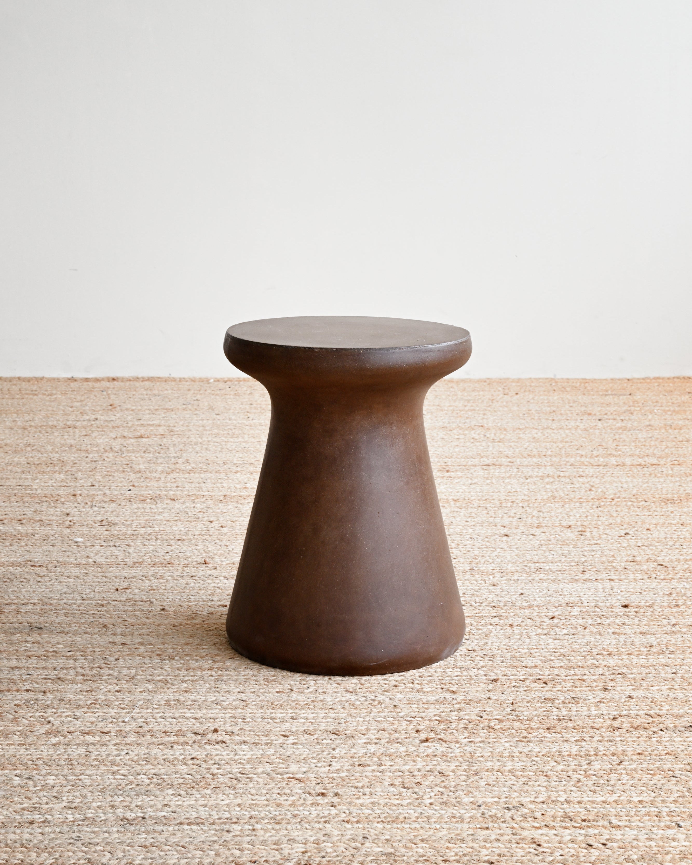 Brown wooden stool on a textured beige surface with a light gray background